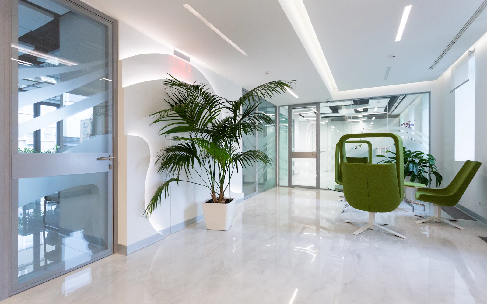 Sala de espera clara, com poltronas verdes e plantas